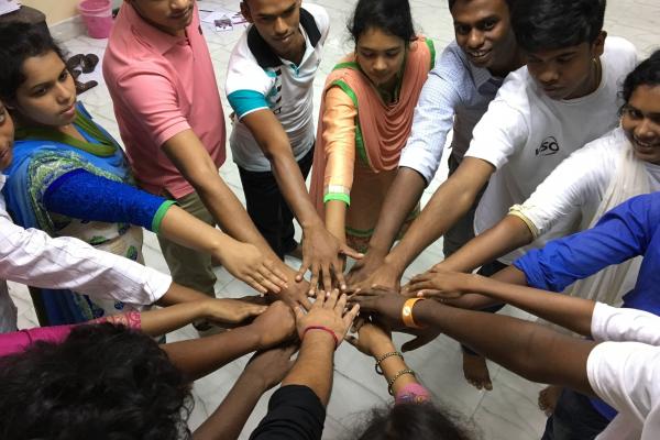 A group of Bangladeshi young people stand in a circle and place their hands in the centre