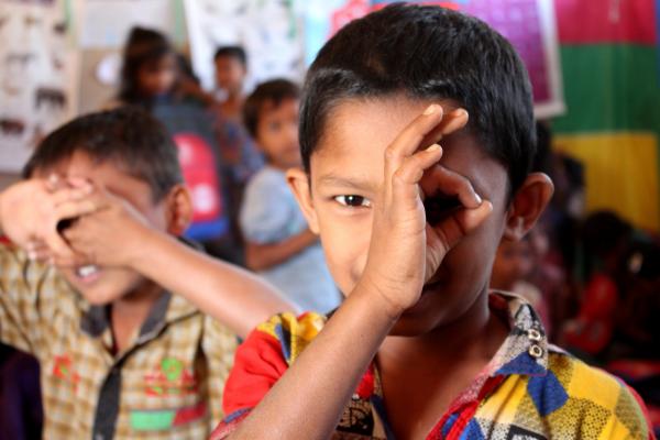 A young Rohingya refugee holds his hand to his face as he plays in a VSO-constructed chilld-friendly space