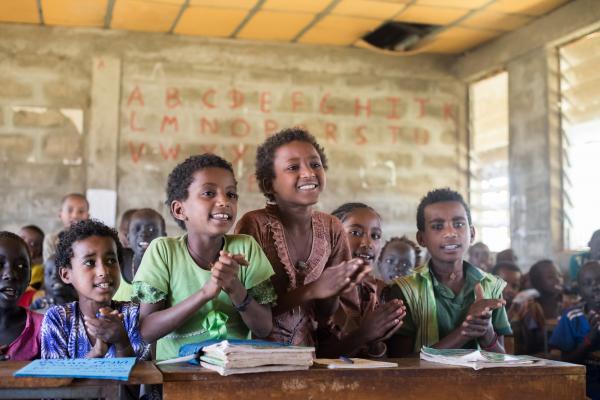 Children sing and clap happily in a busy classroom