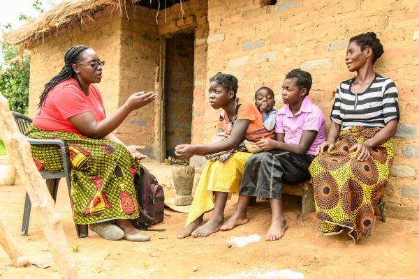 Volunteer Monica Atim sits outside with two teenage girls, a baby and a woman, discussing contraception