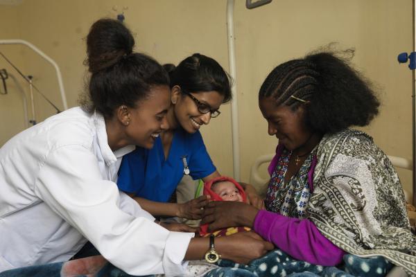 A midwife and a VSO volunteer help a mother to position her newborn baby comfortably