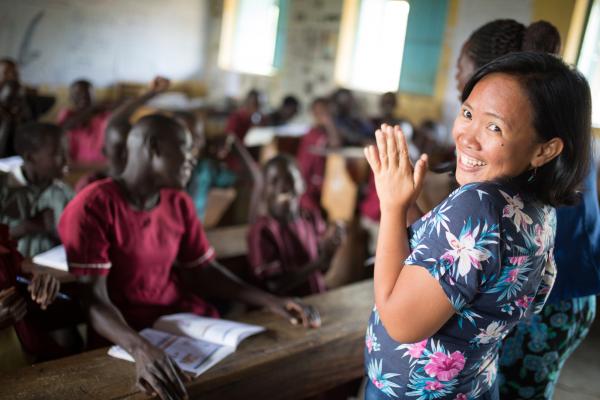 Volunteer Janice Ann Perez turns and smiles as she stands at the front of a full classroom in Karamoja, Uganda