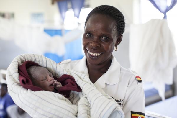 A midwife smiles as she cradles a minutes-old baby wrapped in blankets