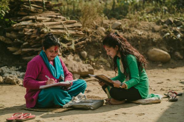 An older woman and a teenage girl sit outside on the ground in Nepal, studying