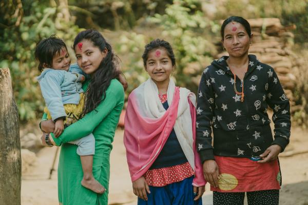 Nirmala holds her toddler sister while standing outside with her other sister and mother