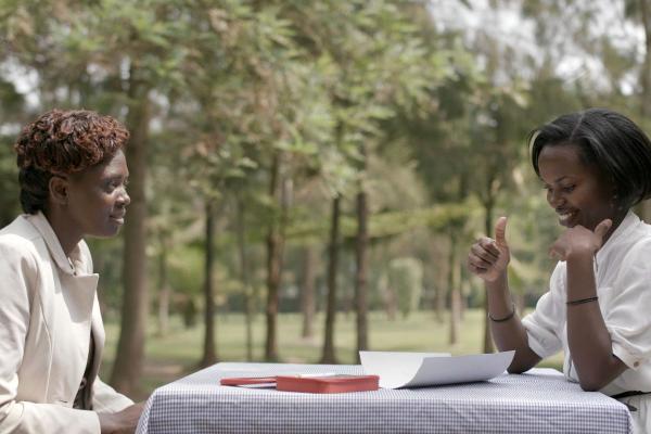 Volunteer Brown Niyonsaba sits across a table from a female health worker, teaching her Rwandan Sign Language