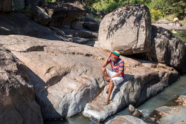 Peer educator JK looks reflective as he sits on a large rock by a river close to his home in Chavani, Masvingo province