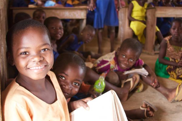 Young children smile as they sit on the floor of their classroom