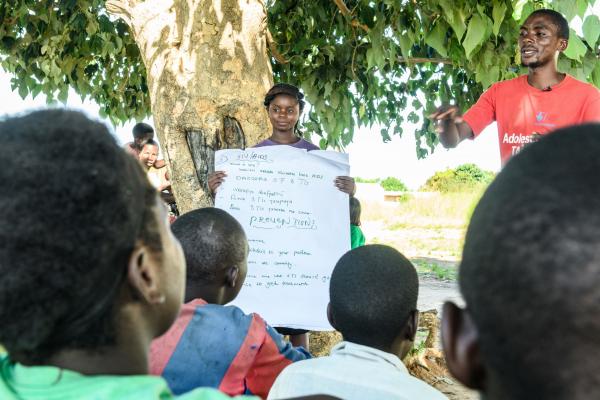 A young woman holds up a sheet of paper for a group, as Alfred delivers a peer education session