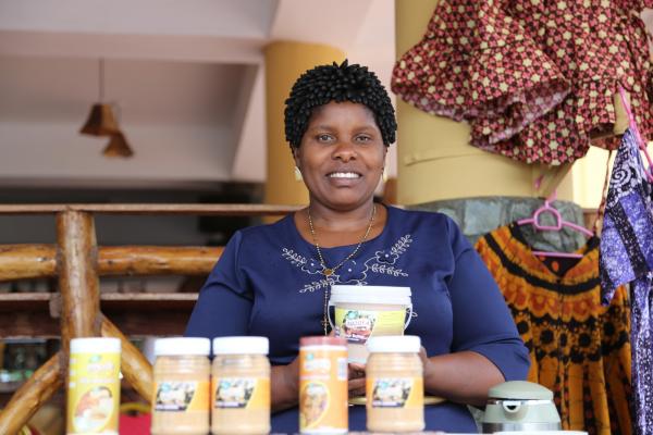 A woman sits holding a tub of peanut butter, with more tubs in front of her