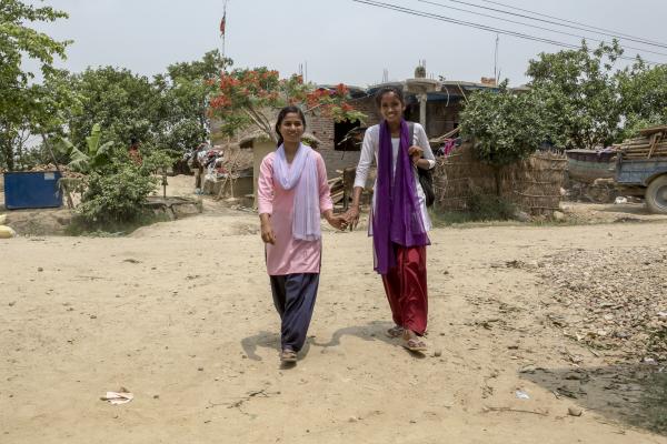 A young woman and a teenage girl smile as they walk hand-in-hand outside in a village in Nepal