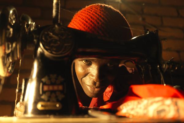 A tailor peers through her sewing machine as she works by solar-powered lamplight
