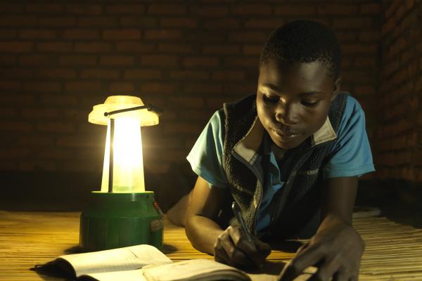 A young boy lies on the floor and does his homework by the light of a solar lantern