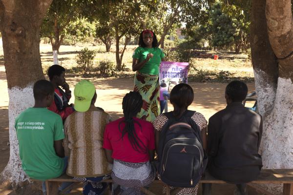 A group of community volunteers sit and listen to a woman speaking