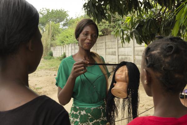 Merenciana uses a mannequin to demonstrate her hair braiding to two women
