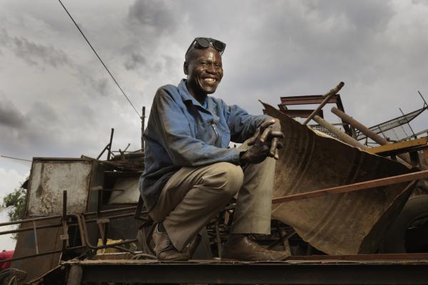 Arthur smiles as he sits atop some scrap metal in his welding yard