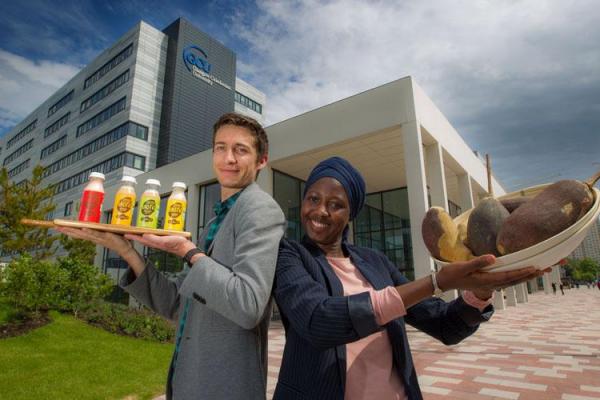 Former volunteer Paul Blackler and his wife Isaotu stand outside an office building, holding fruits and bottles of juice