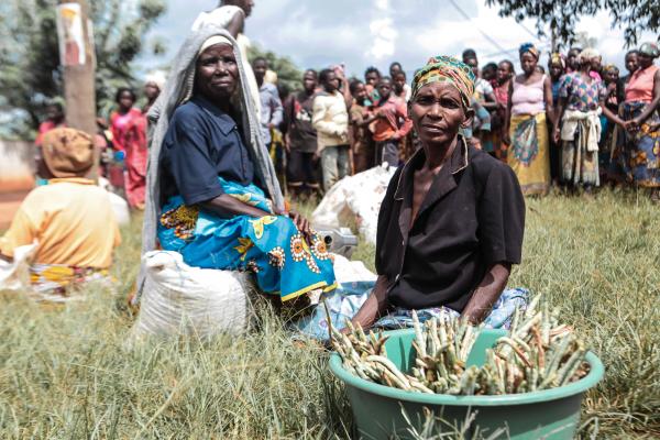 Two women sit in the long grass after receiving food products in Manica province