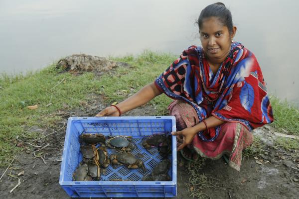 A woman next to a river showing crabs she has caught