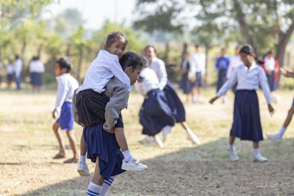 A schoolgirl carries a younger girl on her back as they play outside with a group of children