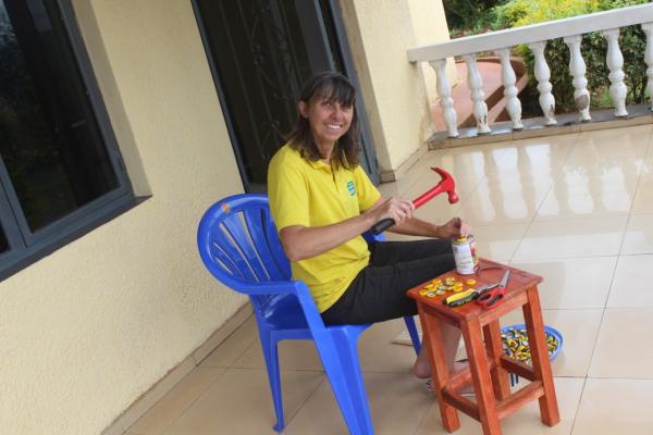 a women sat outdoors smiling on a chair with a hammer and bottletops 