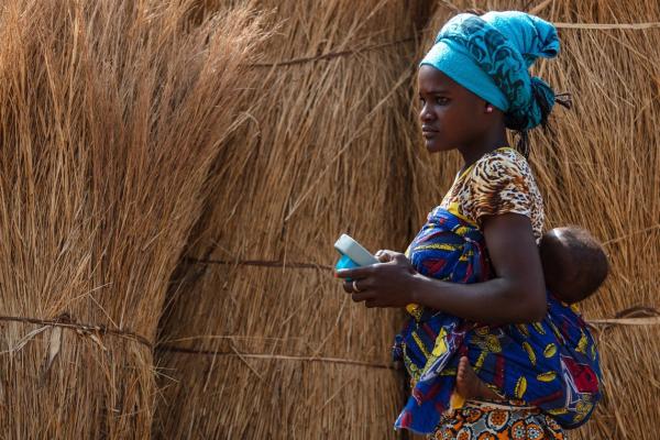 A young mother with her baby on her back uses an Amplio Talking Book in Ghana