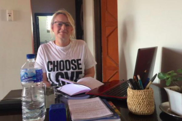 a woman sat at a desk with laptop, smiling at the camera