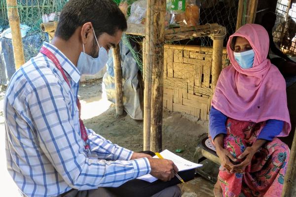 a man and woman sat down wearing facemasks. The man is carrying out a questionnaire on the woman.