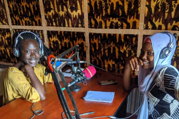 Two young women sit at a desk with radio microphones and headphones