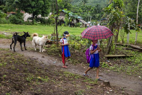 Children in Myanmar walk across a field to get to school.
