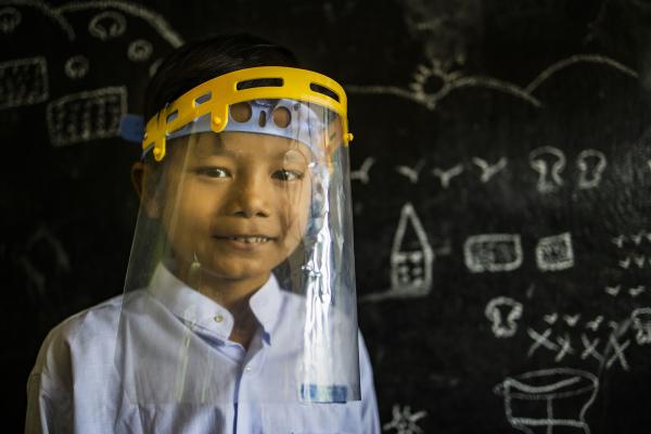 Student Phyo Ko Ko stands in front of a blackboard in a Burmese classroom. 