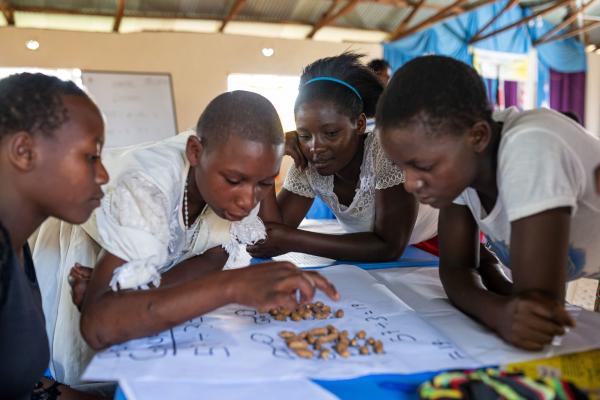 Four girls huddle together around a table and use peanuts to practise maths skills