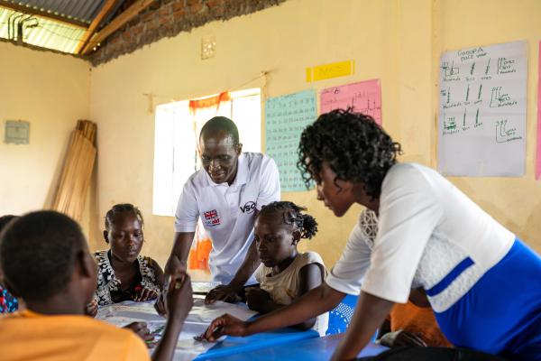 Volunteer Peter and teacher Jackline help some girls who are working together at a large table