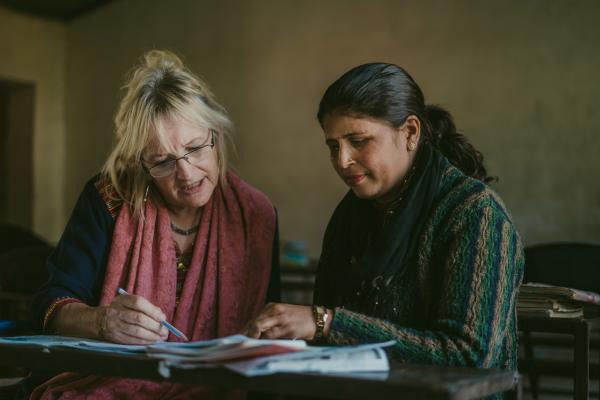 Volunteer Anne and a local schoolteacher sit at a classroom desk, looking at students' work together