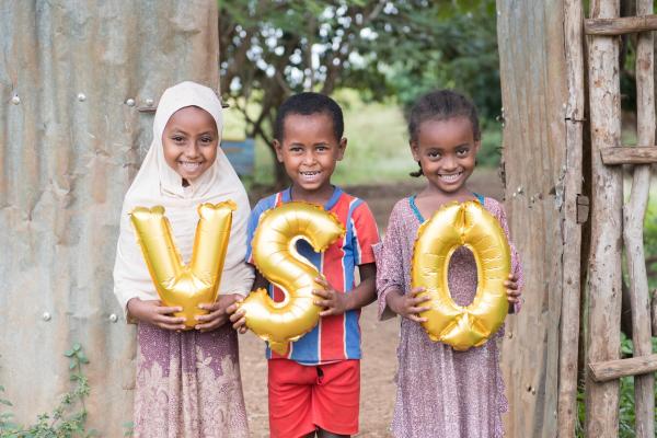 Children hold balloons in front of a wooden gate in Ethiopia.