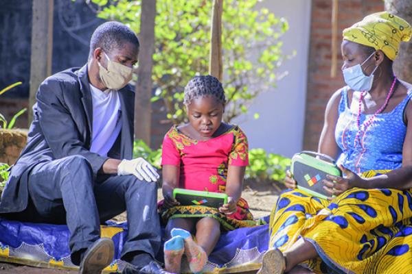 Child working on laptop with parents. Malawi.