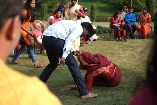 Two actors performing to raise awareness of gender-based violence in Nepal - a man in a white shirt stands aggressively over a woman in a red sari lying on the floor