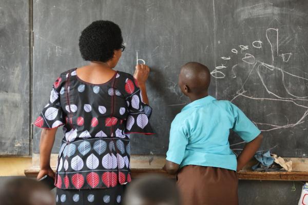 Woman instructs child at chalkboard. Rwanda