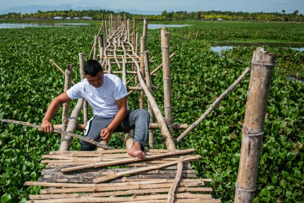 Man building bridge from wood poles