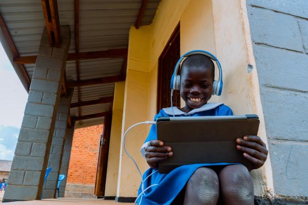 Student Alinafe sits on a step and smiles while using a tablet