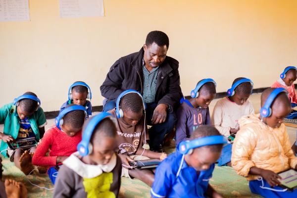 Theonas sits in the learning centre helping students on their tablets