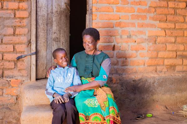 Lonjezo sits with his grandmother on the doorstep of his home