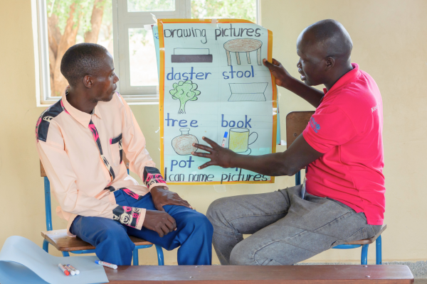 Volunteer Alfred shows teacher Elijah how to create learning materials for his class