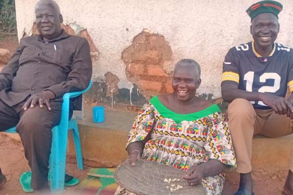 VSO volunteer Alfred sat outside his home with his uncle and aunt.