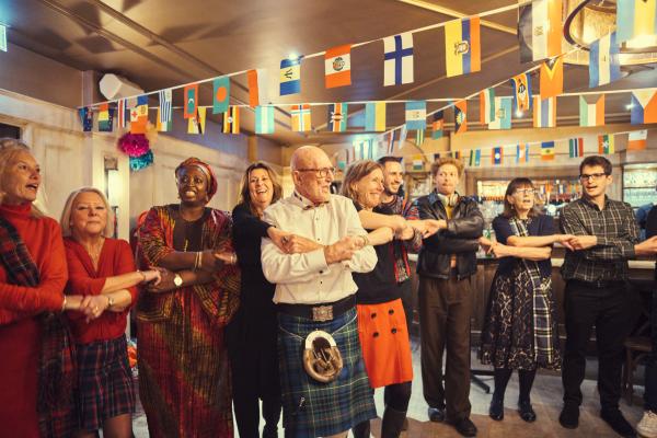 Andrew holding hands and laughing with his friends including Tunde, at his 80th birthday celebration
