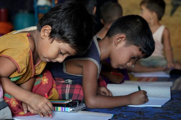 Rohingya children draw pictures in a home-based child-friendly centre in the Cox's Bazar camp, Bangladesh. Two young Rohingya boys sit on the floor of a child-friendly centre in the Cox's Bazar camp, drawing with colouring pencils