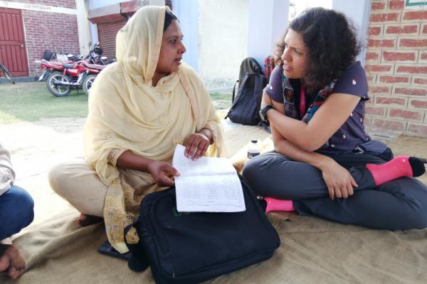 Two women sat on the floor outside, in conversation and holding papers
