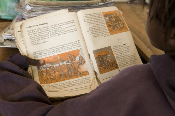 Boy in classroom holds tatty textbook Boy in classroom holds tatty textbook