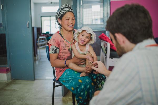 Laxmi plays on her mother's knee while being tended to by Dr. Harry Lynch