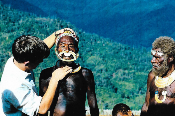 Dr. Nick Maurice on placement with VSO. Two men stood in front of a hilly, countryside view. One man is wearing a traditional local headdress and the other is UK volunteer.